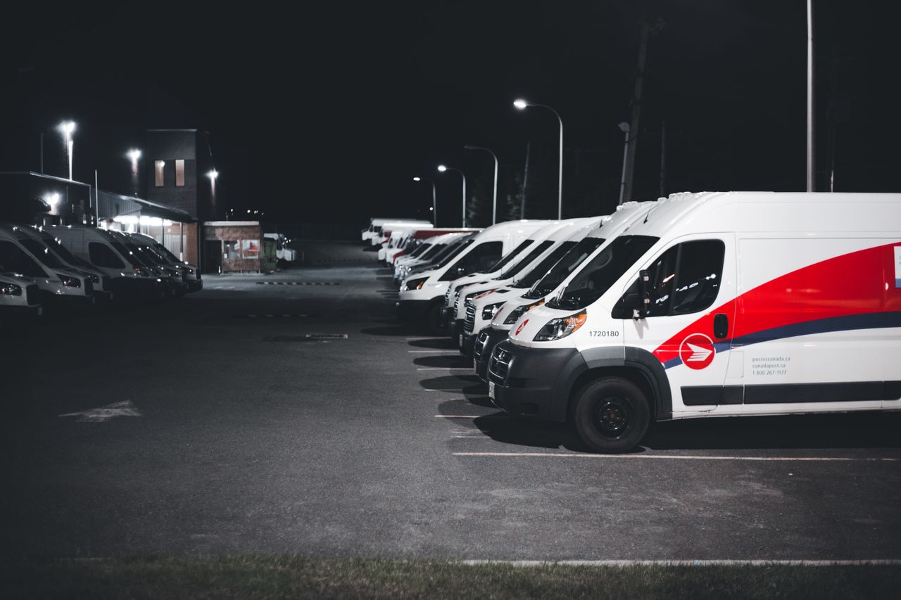 services-04 A lineup of white and red delivery vans parked in a lot under streetlights at night.