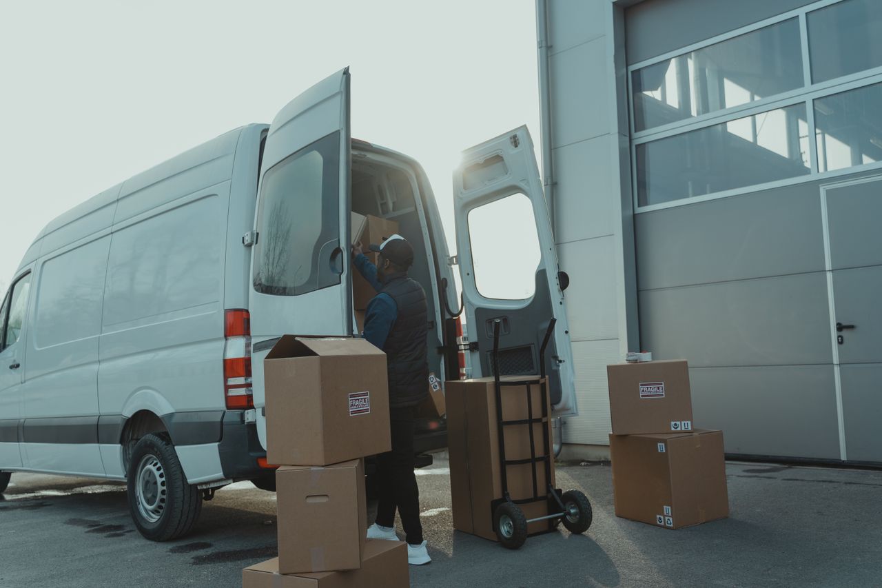 services-01 Courier loading cardboard boxes into a delivery van outside a warehouse.