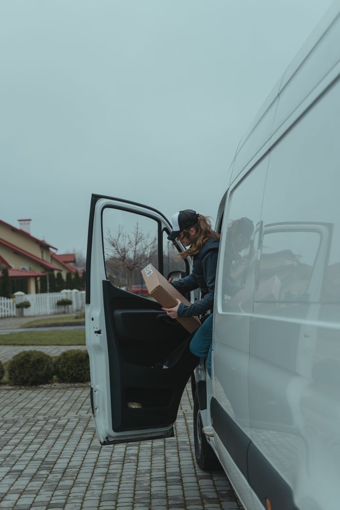 services-02 A delivery person handling packages by a van on a cloudy day.